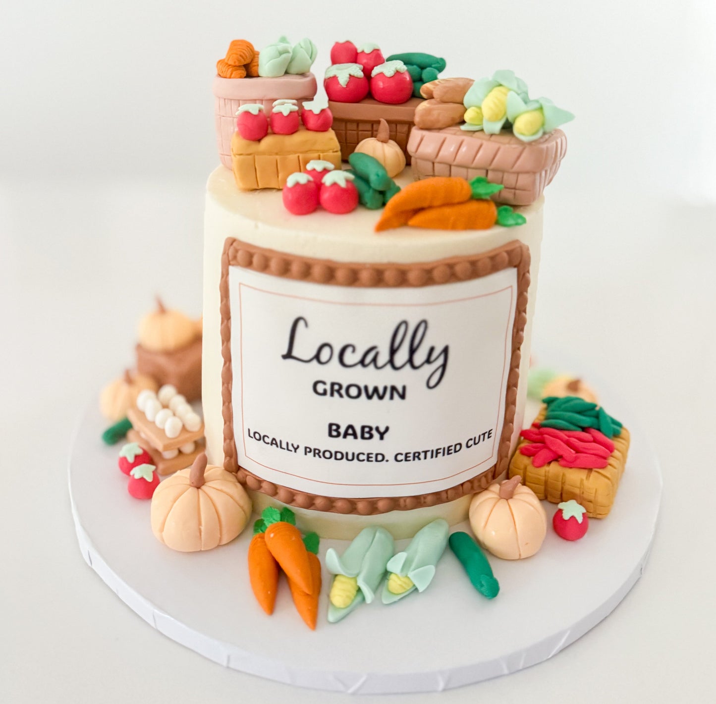 Cake decorated with vegetables and a sign saying 'Locally Grown Baby' on a white background